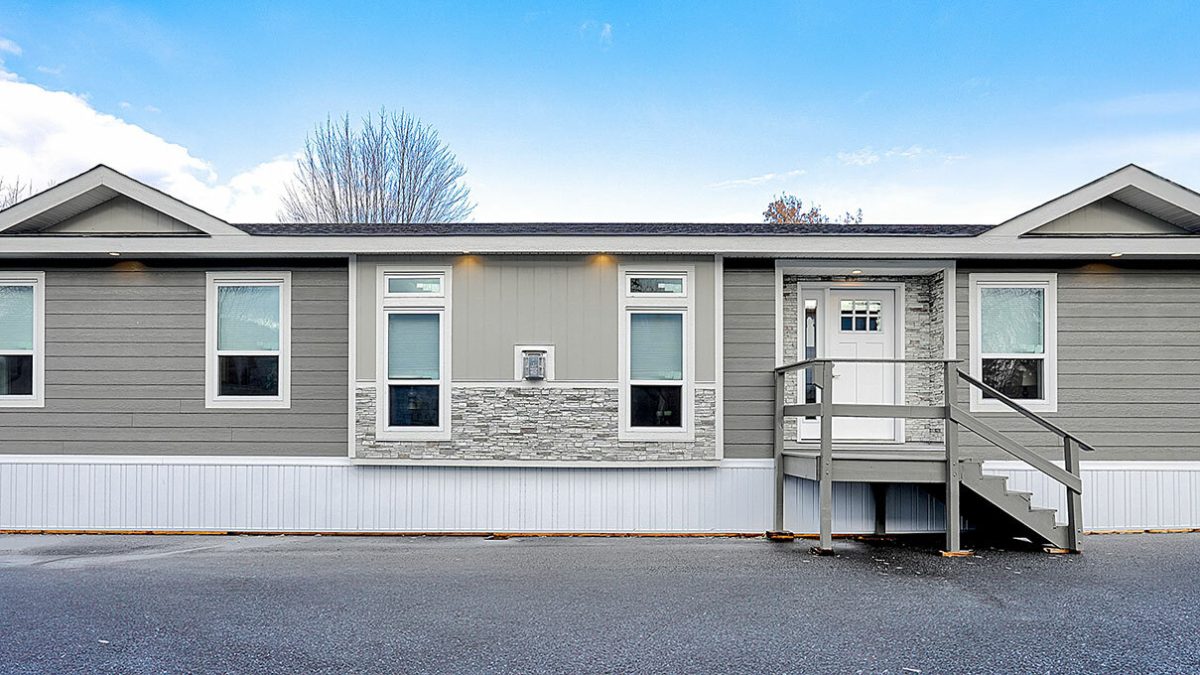 A gray mobile home featuring a porch and stairs, set against a clear sky, showcasing a welcoming outdoor space